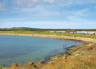 Children paddling in the shallow, calm sea on the beach at Elie Holiday Park, Shell Bay on a sunny day